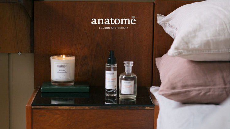 anatomē London Apothecary sleep and wellbeing products featuring a scented candle, pillow spray and botanical formulation beside a bed