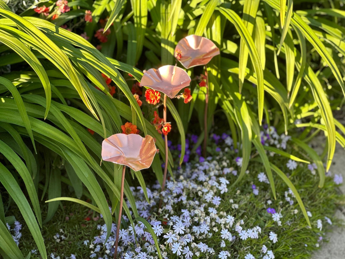 Handmade copper garden flowers by Copper and Green displayed amongst lush green foliage and colourful flowers in a British garden