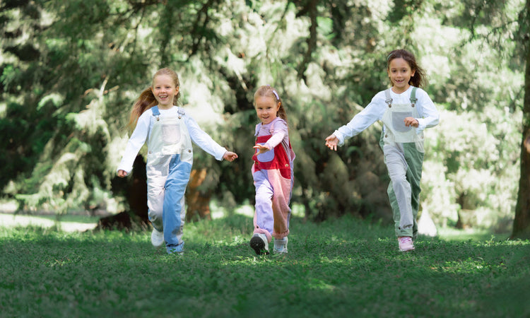 Three children running outdoors wearing colourful Dotty Dungarees patchwork dungarees