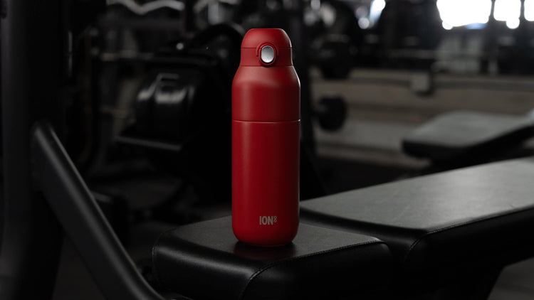 Red ION8 leakproof reusable water bottle in a gym