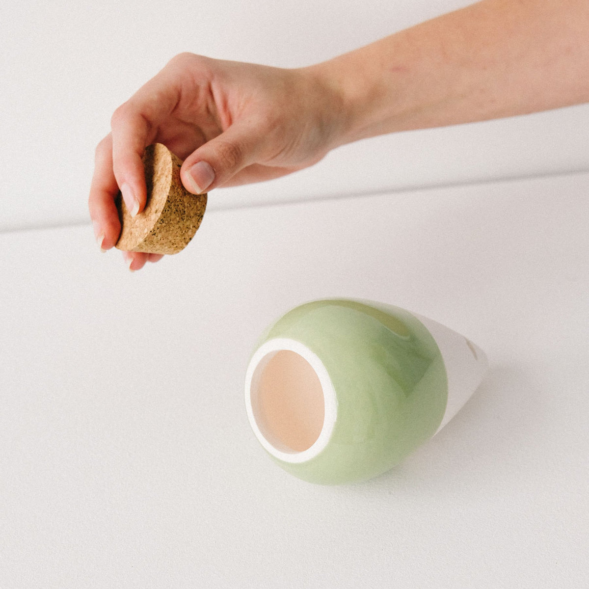 Hand lifting the cork stopper from a sage green Pepin Olla