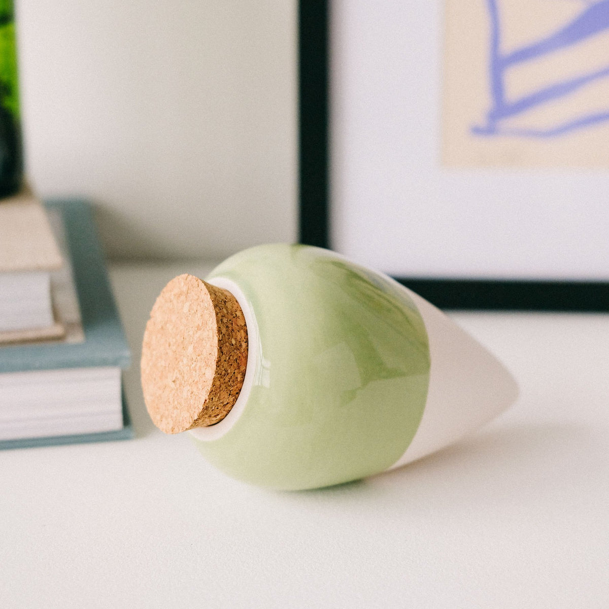 Sage green Pepin Olla with cork stopper lying on a white shelf