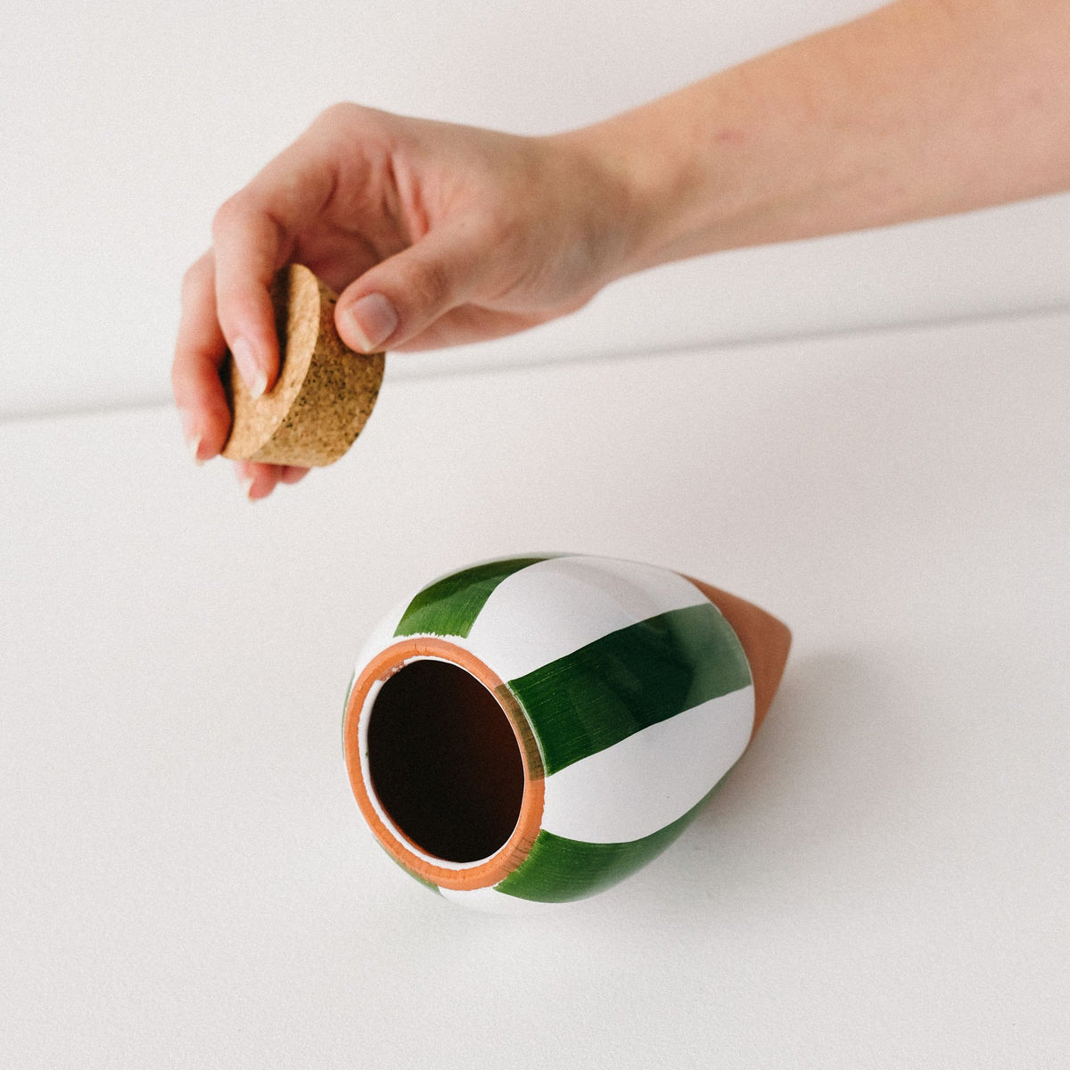 Hand lifting the cork stopper from a green and white striped Pepin Olla