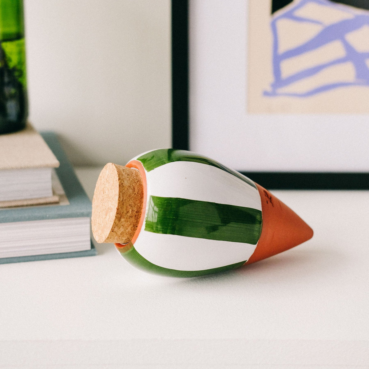 Green and white striped Pepin Olla with cork stopper lying on a white shelf