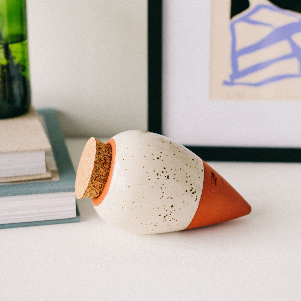 Speckled white Pepin Olla with cork stopper lying on a white shelf