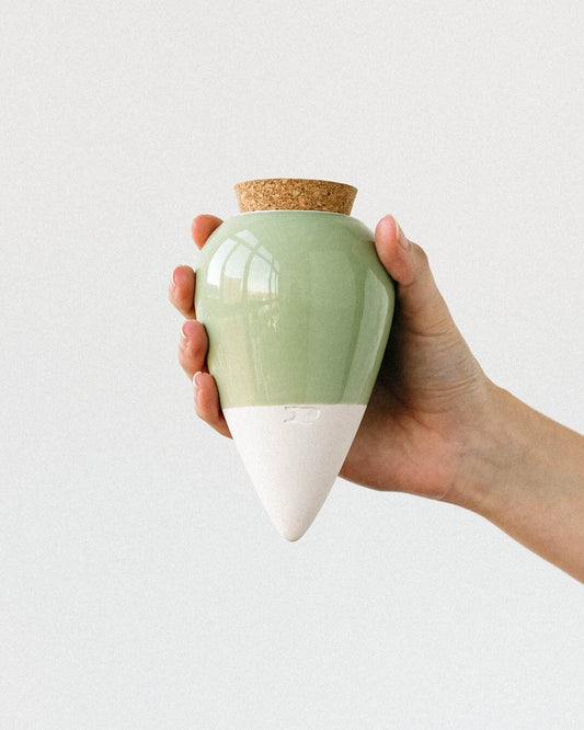 Pepin Olla with sage green glazed top and white base, held in the hand