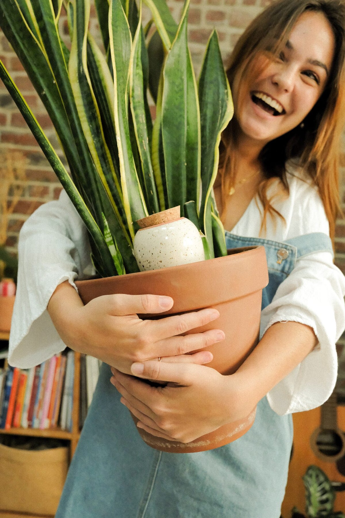 Smiling woman holding a potted snake plant watered by a speckled white Pepin Olla