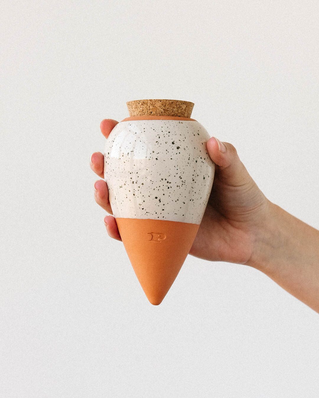 Pepin Olla with speckled white glazed top and terracotta base, held in the hand