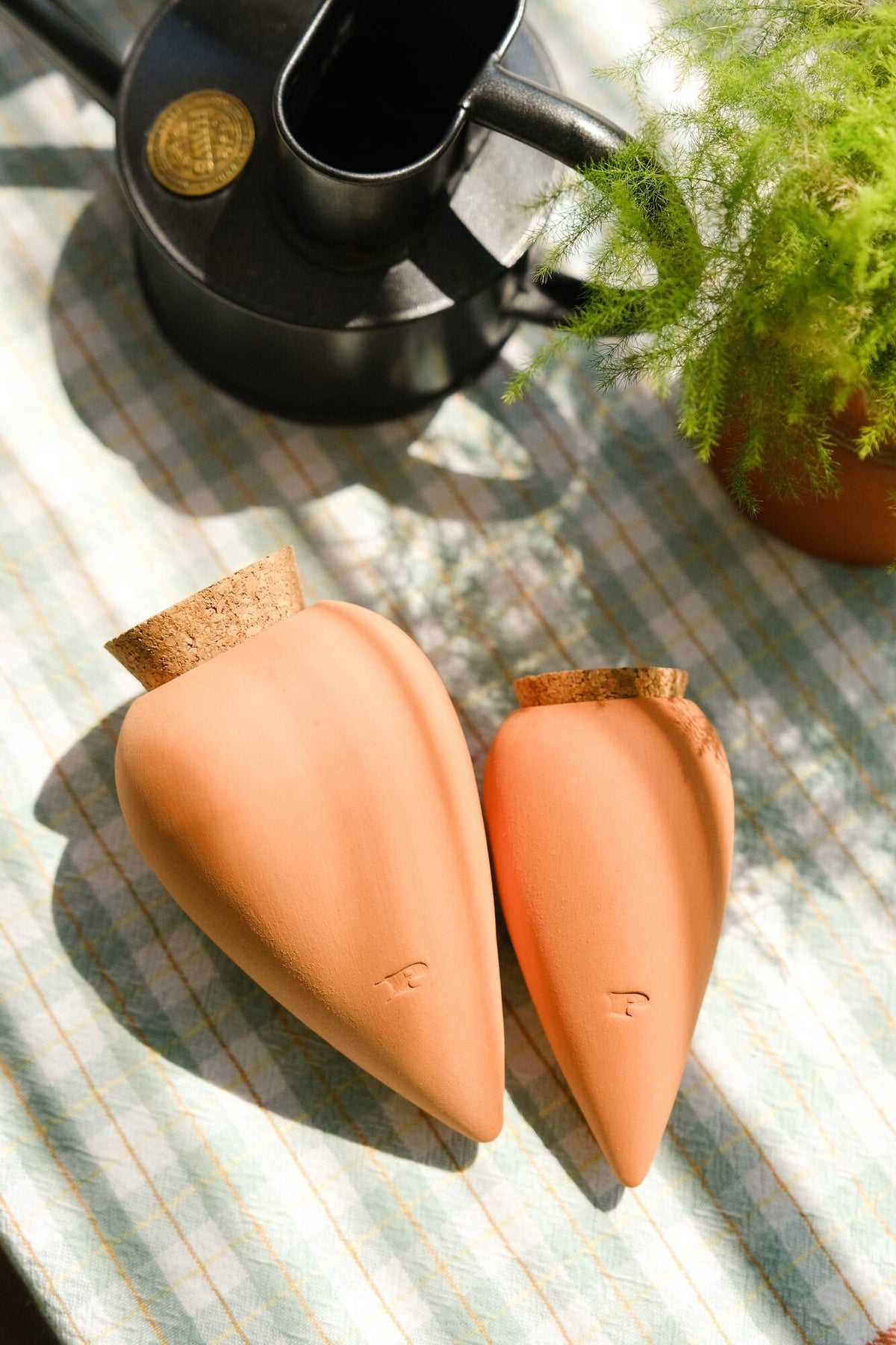 Two terracotta Pepin Ollas with cork stoppers lying on a table beside a watering can